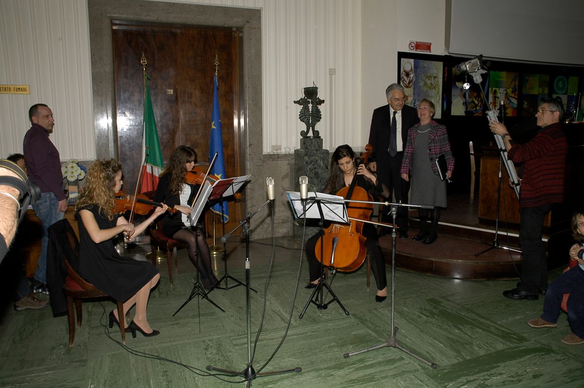 Aula magna dell'ISS, durante la prima edizione de: "Il Volo di Pègaso", anno 2009; trio del Conservatorio di Santa Cecilia (da sinistra) Guendalina Pulcinelli, primo violino; Anna Oleandro, secondo violino; Fabrizia Pandimiglio, violoncello; (in piedi sulla destra) il presidente dell'ISS Prof. Enrico Garaci e la direttrice generale dell'ISS, Dr.ssa Monica Bettoni