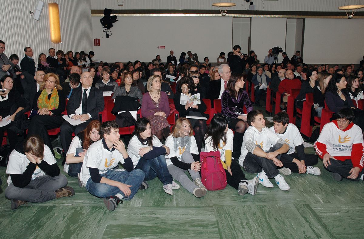 Aula magna dell'ISS, durante la prima edizione de: "Il Volo di Pègaso", anno 2009; ragazzi seduti a terra che indossano le maglie con la scritta "Consulta Nazionale delle Malattie Rare"