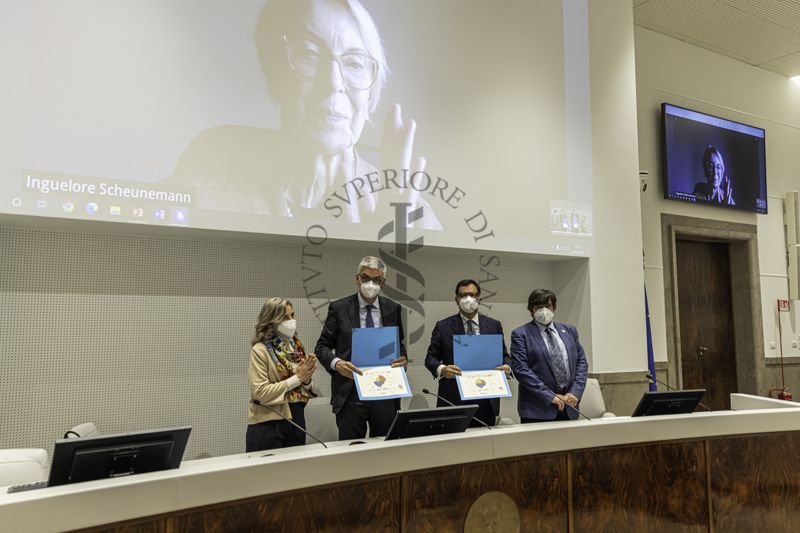 Il Prof. SIlvio Brusaferro, Presidente dell'ISS e il Dr. Andrea Piccioli, Direttore Generale dell'ISS mostrano gli attestati di certificazione HERITY per l'apprezzamento globale della qualità della gestione del Museo e della Biblioteca dell'ISS per gli anni 2021-2023. A sinistra la Dott.ssa Paola De Castro, Direttrice dei Servizi di Presidenza - Conoscenza e Comunicazione Scientifica e a destra il Prof. Maurizio Quagliuolo, Segretario Generale HERITY. Alle loro spalle, la Dott.ssa Inguelore Scheunemann, Presidente HERITY in collegamento video