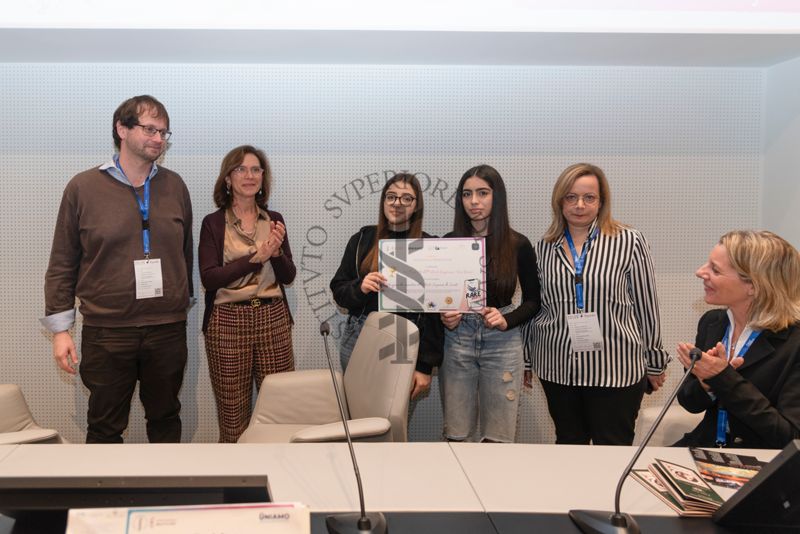 Due ragazze dell'Istituto Comprensivo "Don Diana" di Casal Principe (Caserta) ricevono l'attestato di premiazione "Un giorno da ricercatore all'Istituto Superiore di Sanità". Con loro il Dott. Guido Gigante, ricercatore del Centro Protezione dalle Radiazioni e fisica computazionale dell'Istituto Superiore di Sanità (primo da sinistra), la Dott.ssa. Francesca Cirulli, Direttrice della Ricerca presso il Centro per le Scienze Comportamentali e la Salute Mentale dell'Istituto Superiore di Sanità (seconda da sinistra) e la Dott.ssa Paola Ferrari del Servizio Comunicazione Scientifica, Coordinatrice del Fondo Rari della Biblioteca dell'ISS (sesta da sinistra)