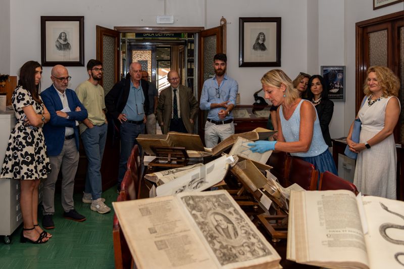 La Dott.ssa Paola Ferrari, Coordinatrice del Fondo Rari della Biblioteca dell'ISS (al centro) illustra agli ospiti alcuni volumi del Fondo Antico. Tra gli invitati ci sono la D.ssa Mirella Taranto, Renponsabile dell'Ufficio Stampa dell'ISS (prima da sinistra), il Prof. Antonio Mistretta, Responsabile del Servizio Comunicazione Scientifica dell'ISS (secondo da sinistra), il Prof. Giovanni Rezza, ex Dirigente dell'ISS e ex Direttore generale della Prevenzione Sanitaria del Ministero della Salute (quarto da sinistra) e il Prof. Antonio Cassone, ex Dirigente di Ricerca e Direttore del Dipartimento di Malattie Infettive, Parassitarie ed Immunomediate dell'ISS (quinto da sinistra)