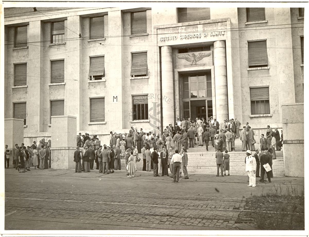 Ripresa di un ampio gruppo di persone davanti all'ingresso principale dell'Istituto Superiore di Sanità, lungo strada e sulle scale, in occasione del ricevimento offerto nel giardino dall'Istituto in occasione del congresso presso la scalinata dell'entrata principale dell'Istituto