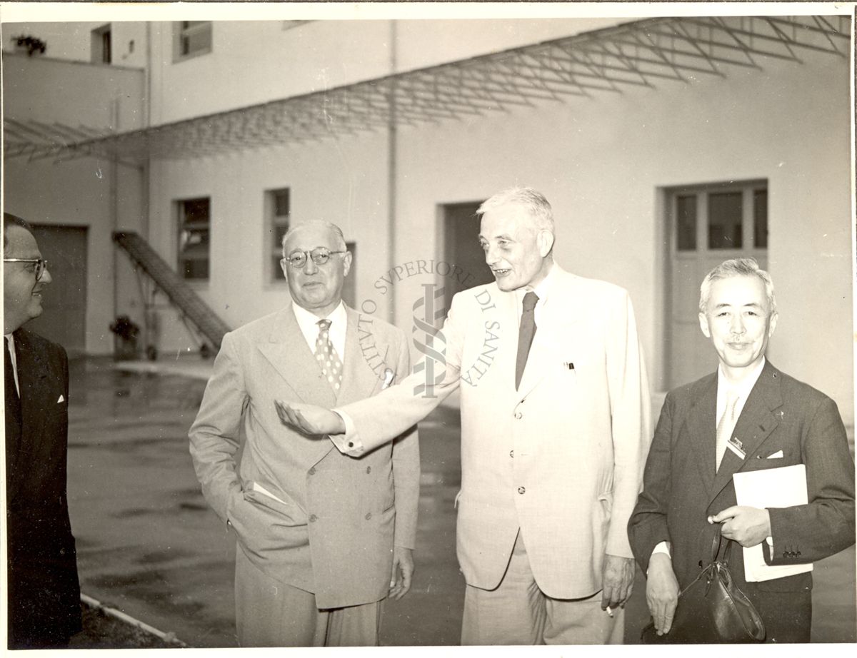 Prof. Marotta (a sinistra), Prof. Kluyver (al centro) e Prof. Kimura (a destra) ripresi all'esterno dell'Istituto Farmacoterapico Italiano durante la visita tenuta in occasione del Congresso. All'estrema sinistra della foto compare il Dott. Penso.