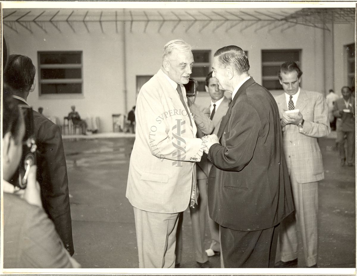 Prof. Kluyver e Dott. Alecce ripresi mentre si stringono la mano circondati da giurnalisti durante la visita all'Istituto Farmacoterapico italiano in occasione del Congresso