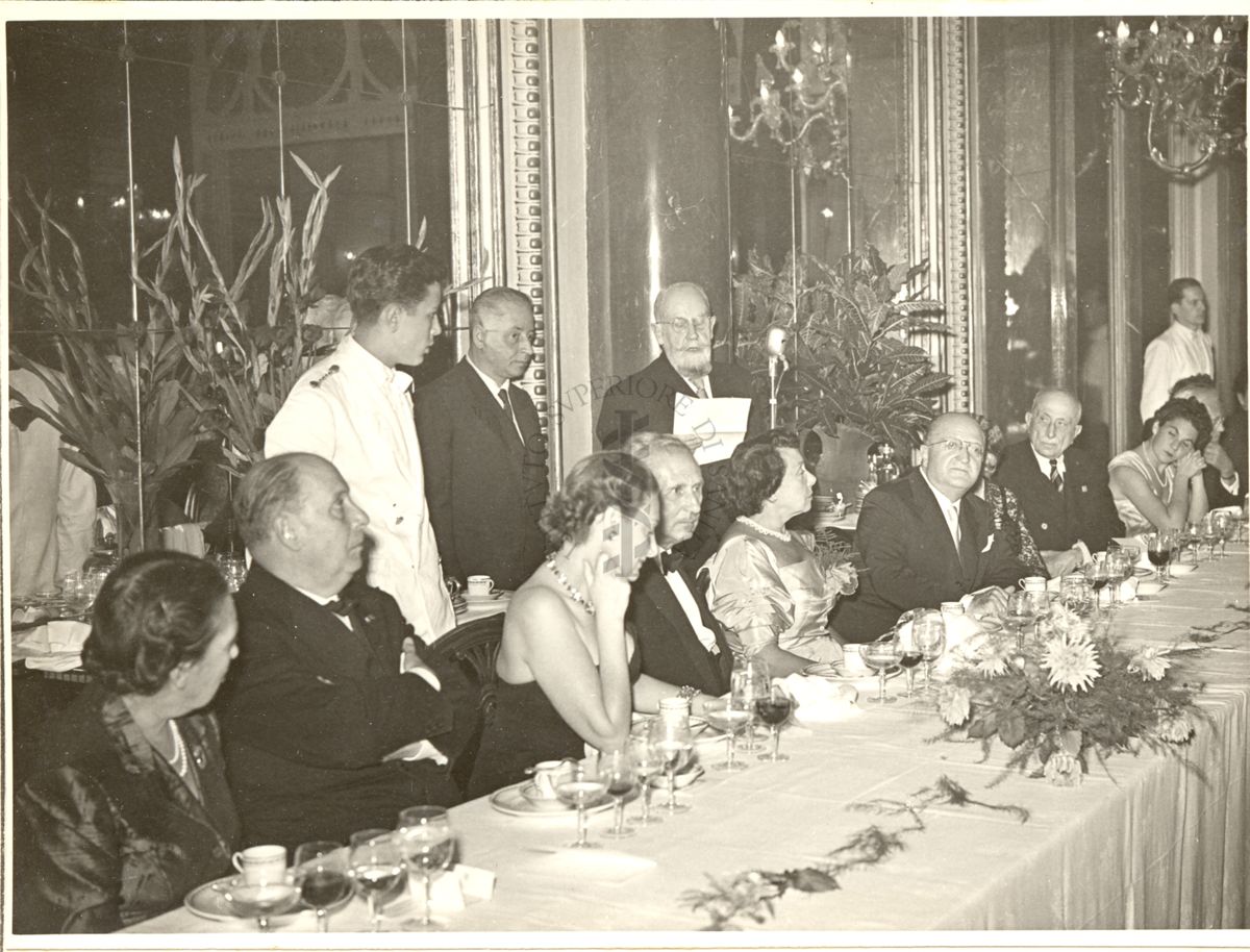 Ripresa del tavolo centrale durante il Pranzo al Grand Hotel di Roma in occasione del Congresso mentre un soggetto tiene un discorso dal microfono. Inquadrato il Sindaco di Roma Rebecchini (secondo da sinistra).