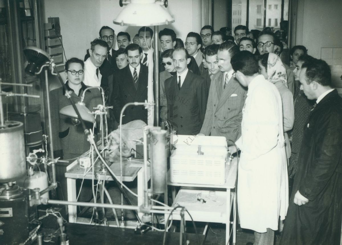 Gruppo di studenti Uruguaiani in un laboratorio dell'Istituto Superiore di Sanità intenti nell'osservazione di un esperimento su cavia. A sinistra, con il camice bianco, sembra presente il Prof. Bovet.
