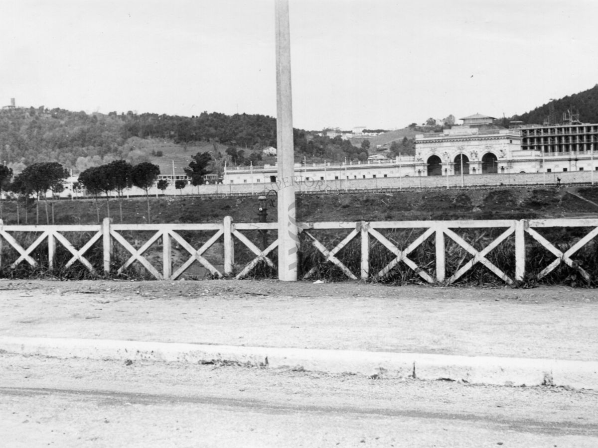 Inquadratura del marciapiede di una carreggiata che corre parallela al Tevere, con il Palazzo Littorio in costruzione sullo sfondo