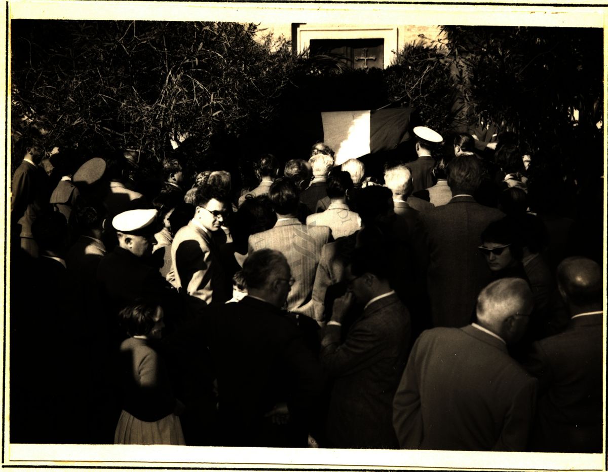 Gruppo di persone di spalle che presenziano la commemorazione del Prof. Grassi. In fondo il tricolore italiano che sovrasta la lapide