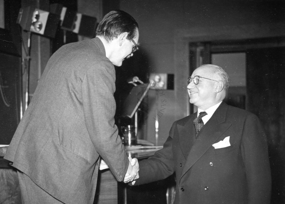 Il Prof. Martin, in posizione rialzata, stringe la mano del Prof. Marotta nell'aula magna dell'Istituto Superiore di Sanità in occasione della Conferenza lì tenuta