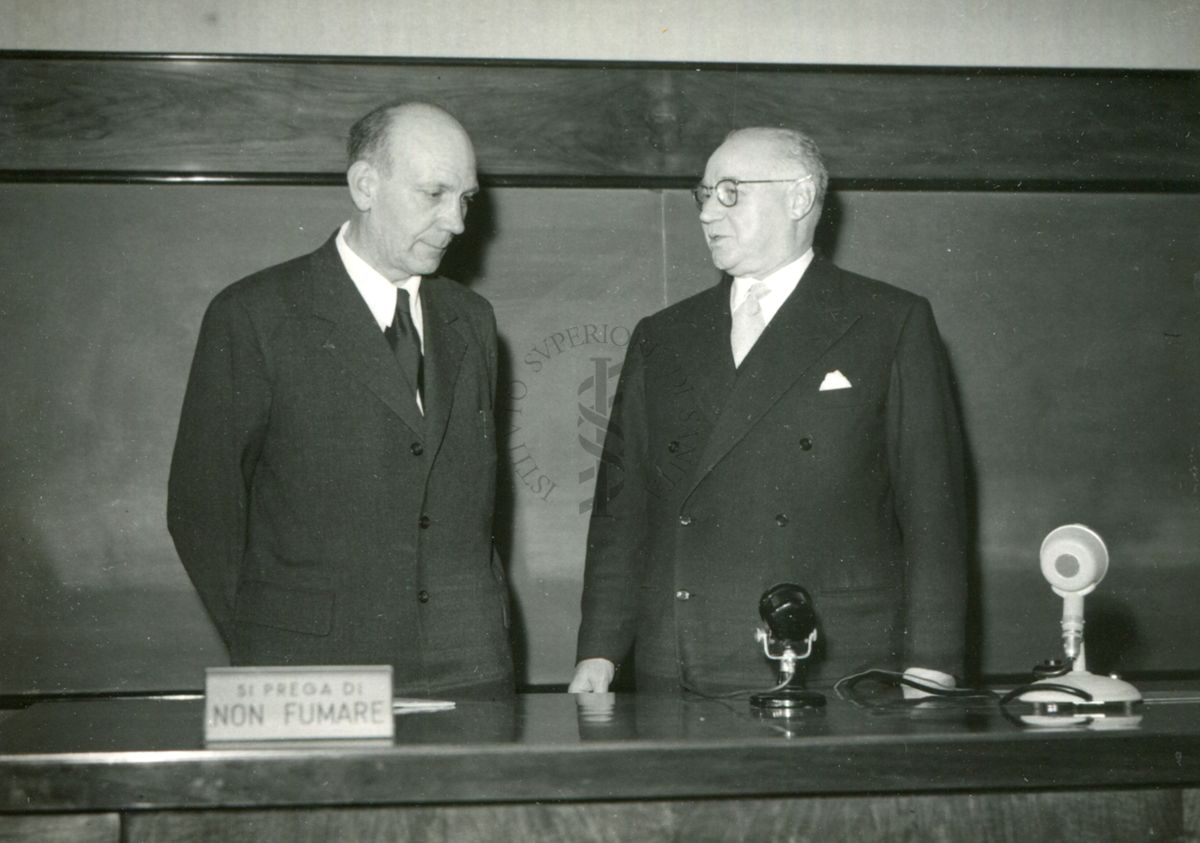 Il Prof. Holter (a sinistra) e il Prof. Bovet ripresi dietro il tavolo dei relatori durante in occasione della conferenza tenuta dal Prof. Holter nell'aula magna dell'Istituto Superiore di Sanità