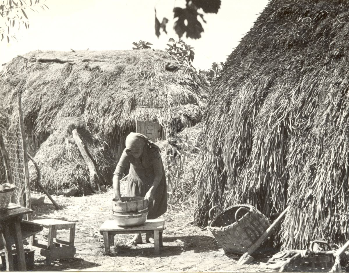 Villaggio di capanne con donna al lavoro.