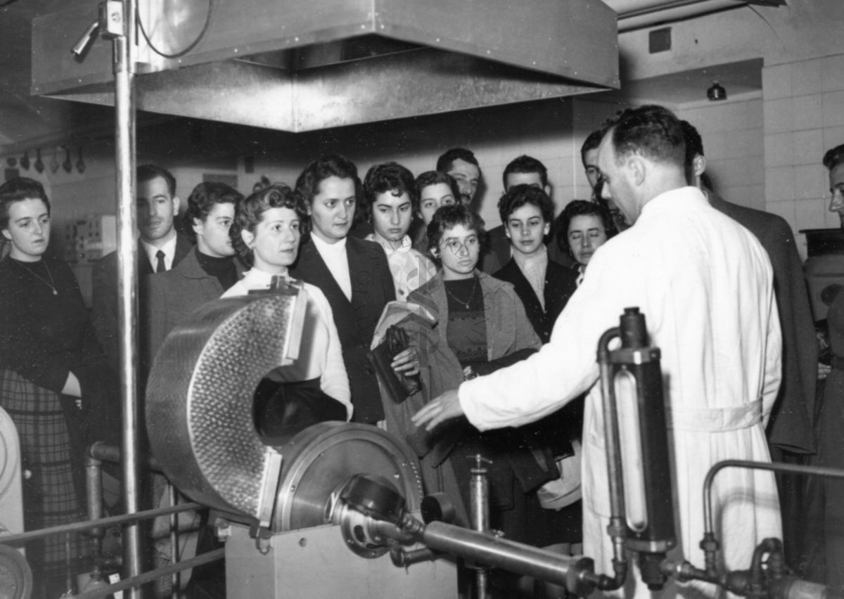 Il gruppo degli studenti uruguaiani in visita all'Istituto Superiore di Sanità all'interno di uno dei laboratori, davanti ad un macchinario presentato da un dipendente dell'Istituto in camice bianco.