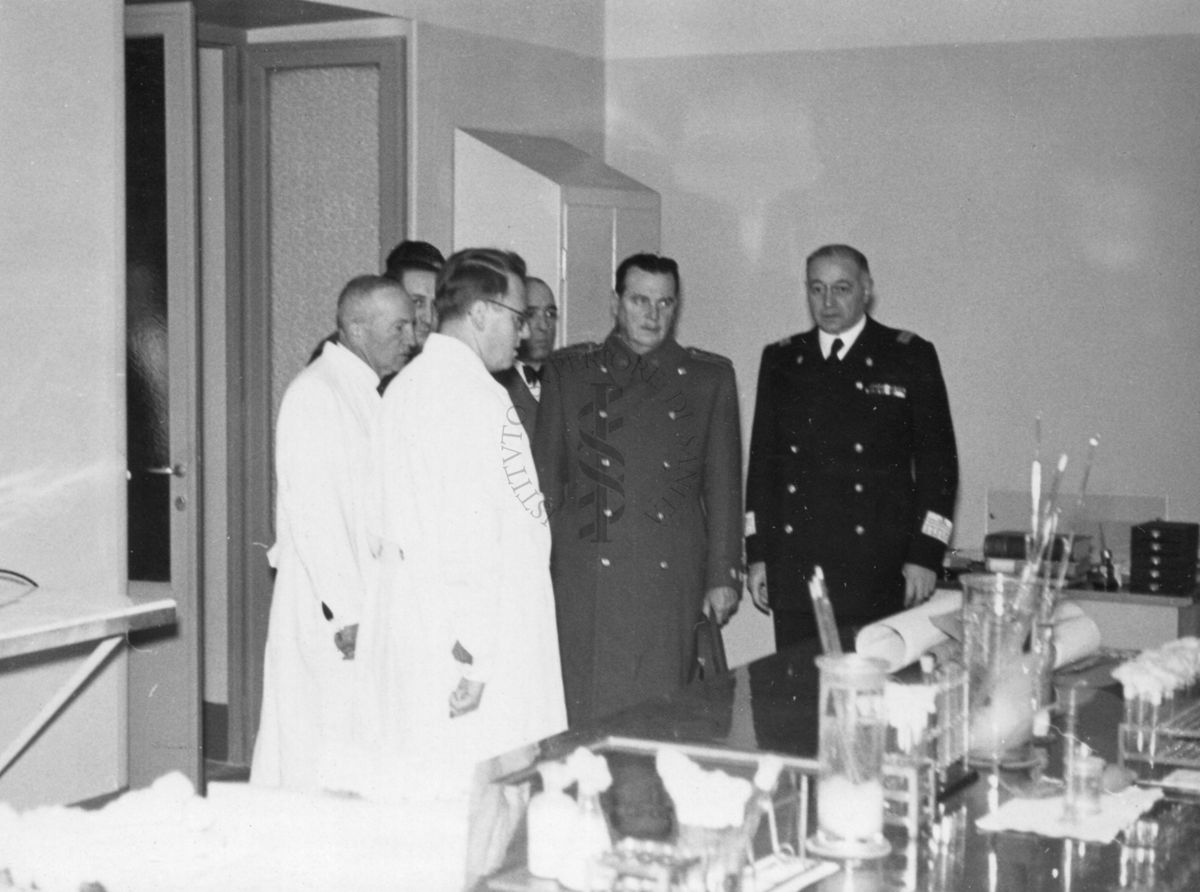 Il Prof. Palanca insieme al Prof. Domenico Marotta (a destra) e ad altre persone in un locale dell'Istituto Superiore di Sanità allestito con vetreria da da laboratorio.