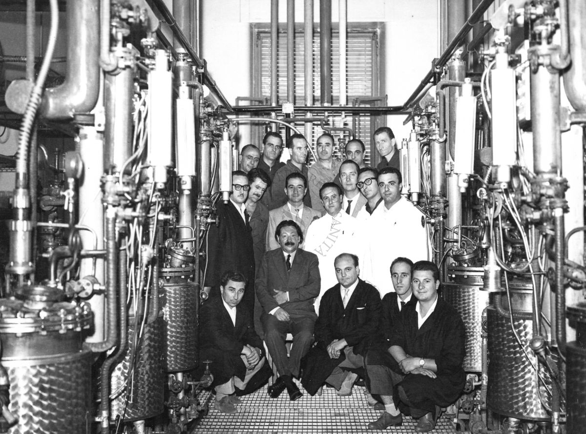 Foto di gruppo con al centro, seduto, il Prof. Ernst Boris Chain, all'interno dell'edificio che ospitava i fermentatori per la fabbricazione della penicillina