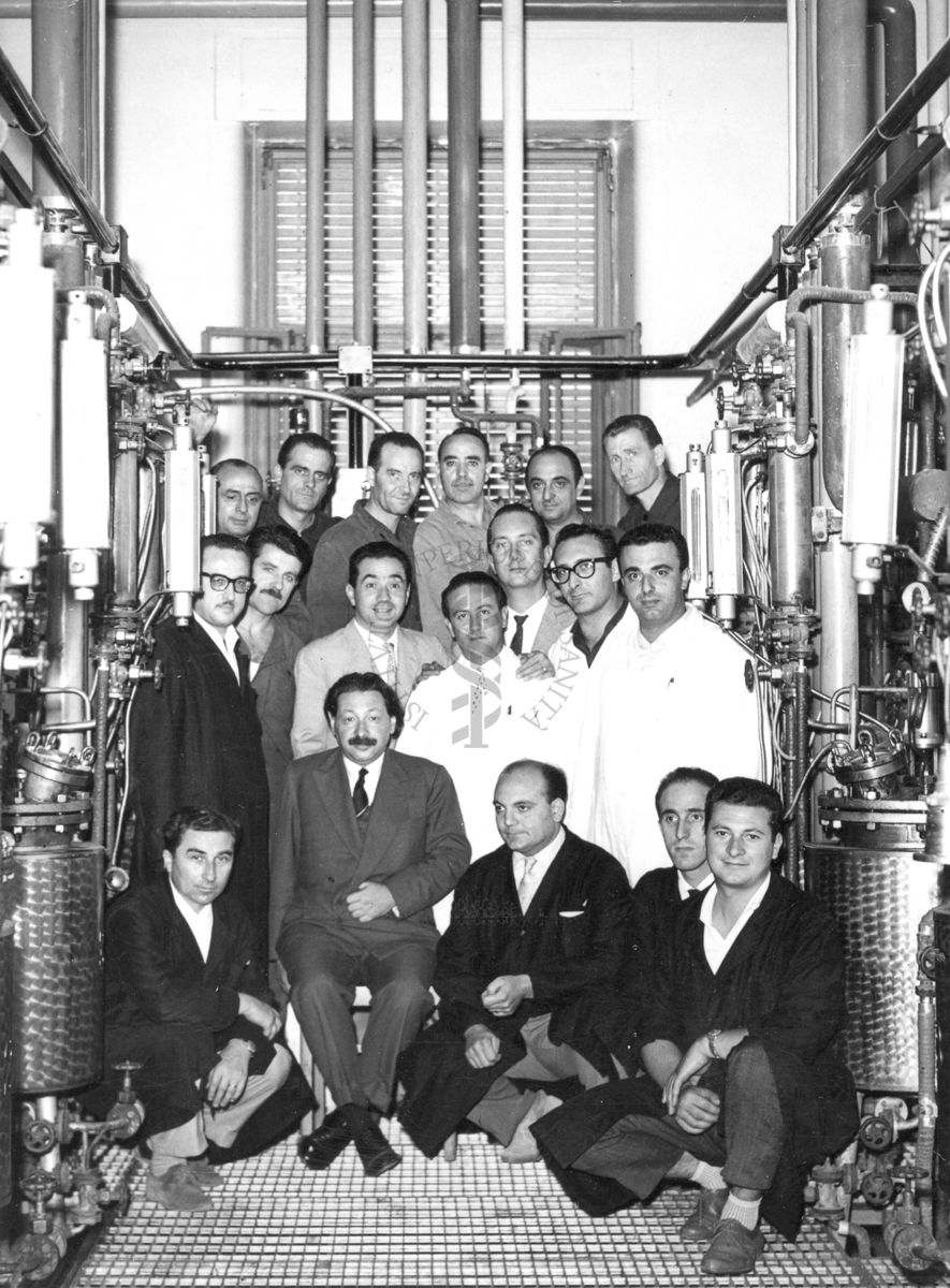 Foto di gruppo con al centro, seduto, il Prof. Ernst Boris Chain, all'interno dell'edificio che ospitava i fermentatori per la fabbricazione della penicillina