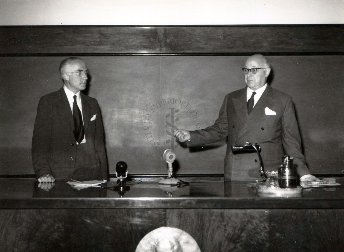 Il prof. Domenico Marotta (lato destro) partecipa alla conferenza in presenza del prof. Mann (lato sinistro) nell'aula magna dell'Istituto Superiore di Sanità. .