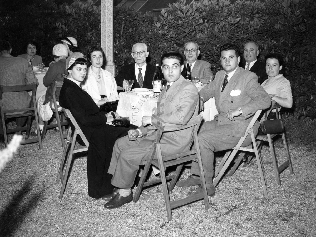 Gruppo di tre donne e cinque uomini in posa seduti ad uno dei tavoli allestiti nel giardino dell'Istituto Superiore di sanità per il banchetto tenuto in occasione del IX Congresso internazionale dell'industria agraria