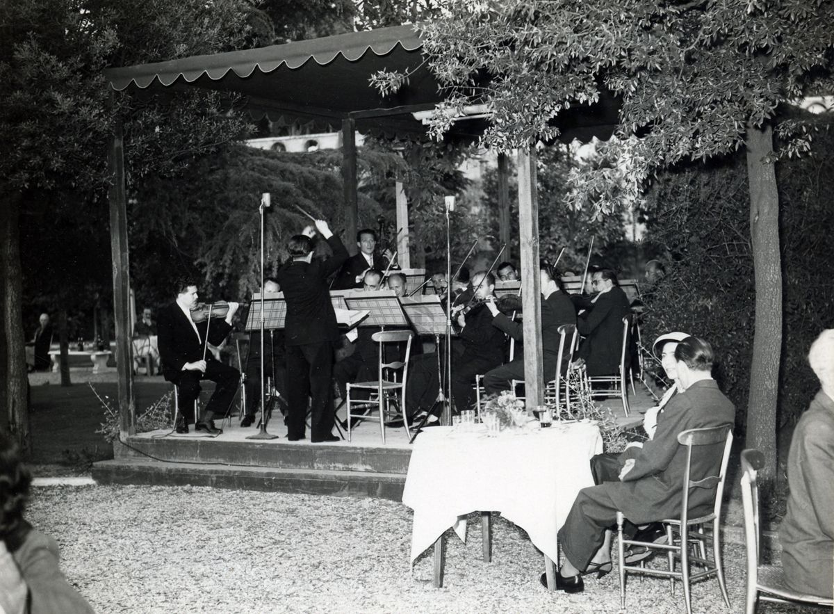 Foto dei musicisti e del loro direttore ripreso di spalle mentre suonano sotto un gazebo, nel giardino dell'Istituto Superiore di Sanità, in occasione del IX Congresso nazionale dell'industria agraria