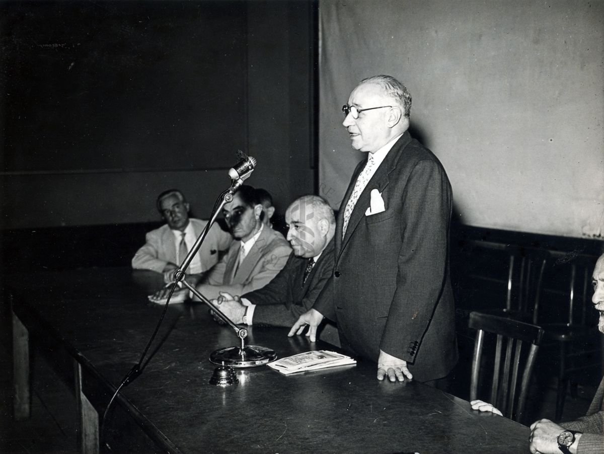 Il Prof. Domenico Marotta in piedi dietro a un tavolo insieme ad altri relatori, intento a parlare ad un microfono, in occasione della conferenza tenuta presso l'Università Popolare Romana
