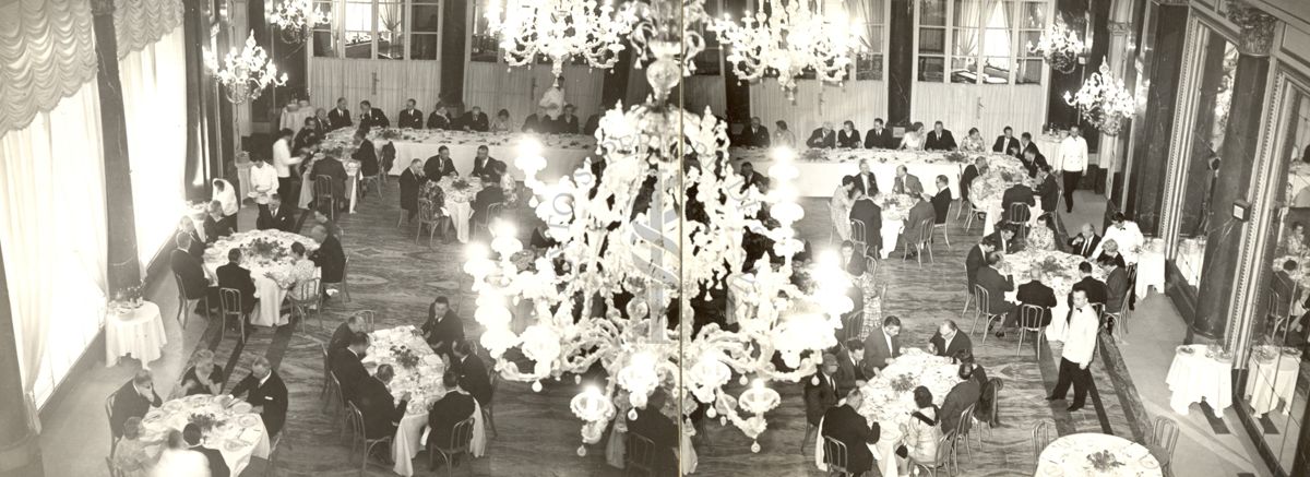 Ripresa dall'alto di una grande sala da pranzo con lampadari di cristallo e tavoli con persone sedute