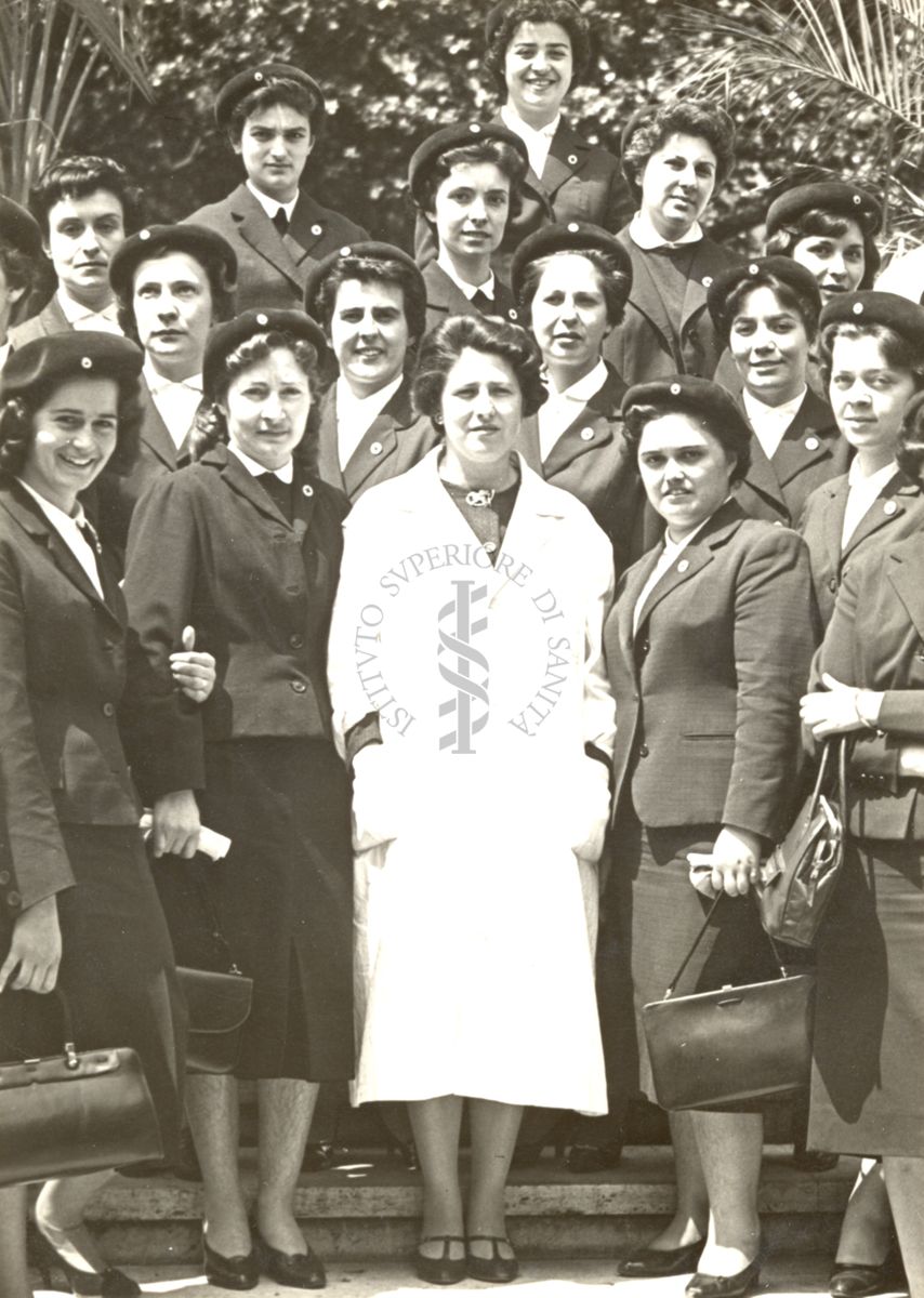 Foto di parte del gruppo delle infermiere della Croce Rossa italiana partecipanti al corso di parassitologia tenuto dall'Istituto Superiore di Sanità presso le scale nel giardino dell'Istituto. Presente una ricercatrice dell'Istituto in camice bianco