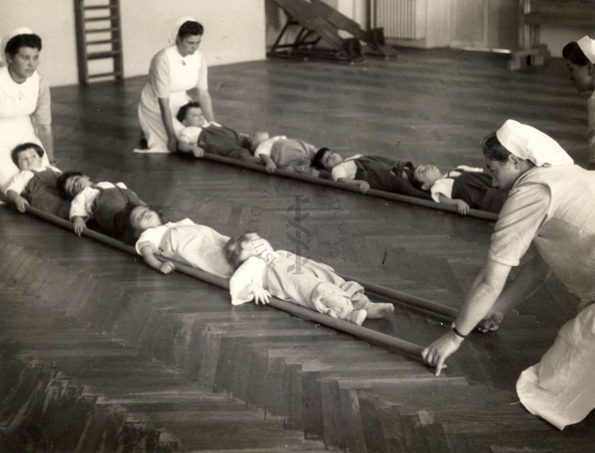 Sala per la ginnastica collettiva dell'Istituto Ortopedico "Luigi Spolverini" di Ariccia (Roma) - delle infermiere sorreggono alcune aste per guidare i movimenti dei bambini