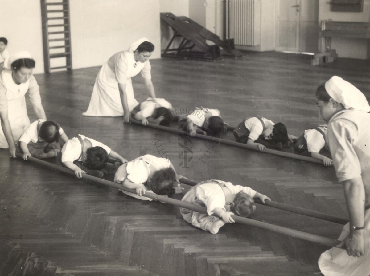 Sala per la ginnastica collettiva dell'Istituto Ortopedico "Luigi Spolverini" di Ariccia (Roma) - delle infermiere sorreggono alcune aste per guidare i movimenti dei bambini