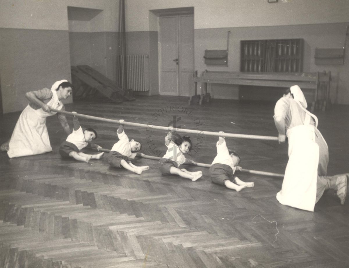 Sala per la ginnastica collettiva dell'Istituto Ortopedico "Luigi Spolverini" di Ariccia (Roma) - delle infermiere sorreggono alcune aste per guidare i movimenti dei bambini