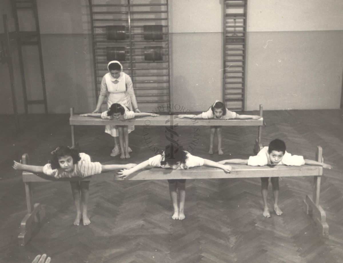 Sala per la ginnastica collettiva dell'Istituto Ortopedico "Luigi Spolverini" di Ariccia (Roma) - un'infermiera controlla la postura di un gruppo di bambini che svolgono esercizi ginnici con l'ausilio di due assi