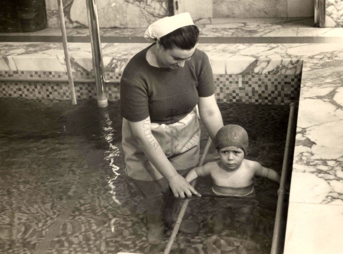 Istituto Ortopedico "Luigi Spolverini" di Ariccia - Infermiera che assiste un bambino alle parallele in piscina