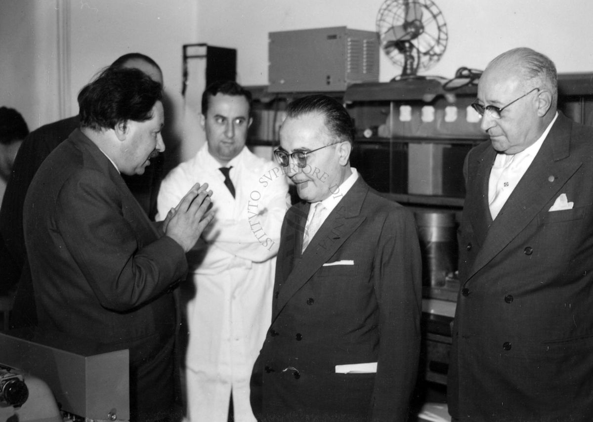 Foto scattata all'interno di uno degli ambienti dell'Istituto Superiore di Sanità, sono presenti da sinistra, il Prof. Ernst Boris Chain che parla con il Ministro della Sanità Vincenzo Monaldi, sulla destra il Prof. Domenico Marotta ed altri