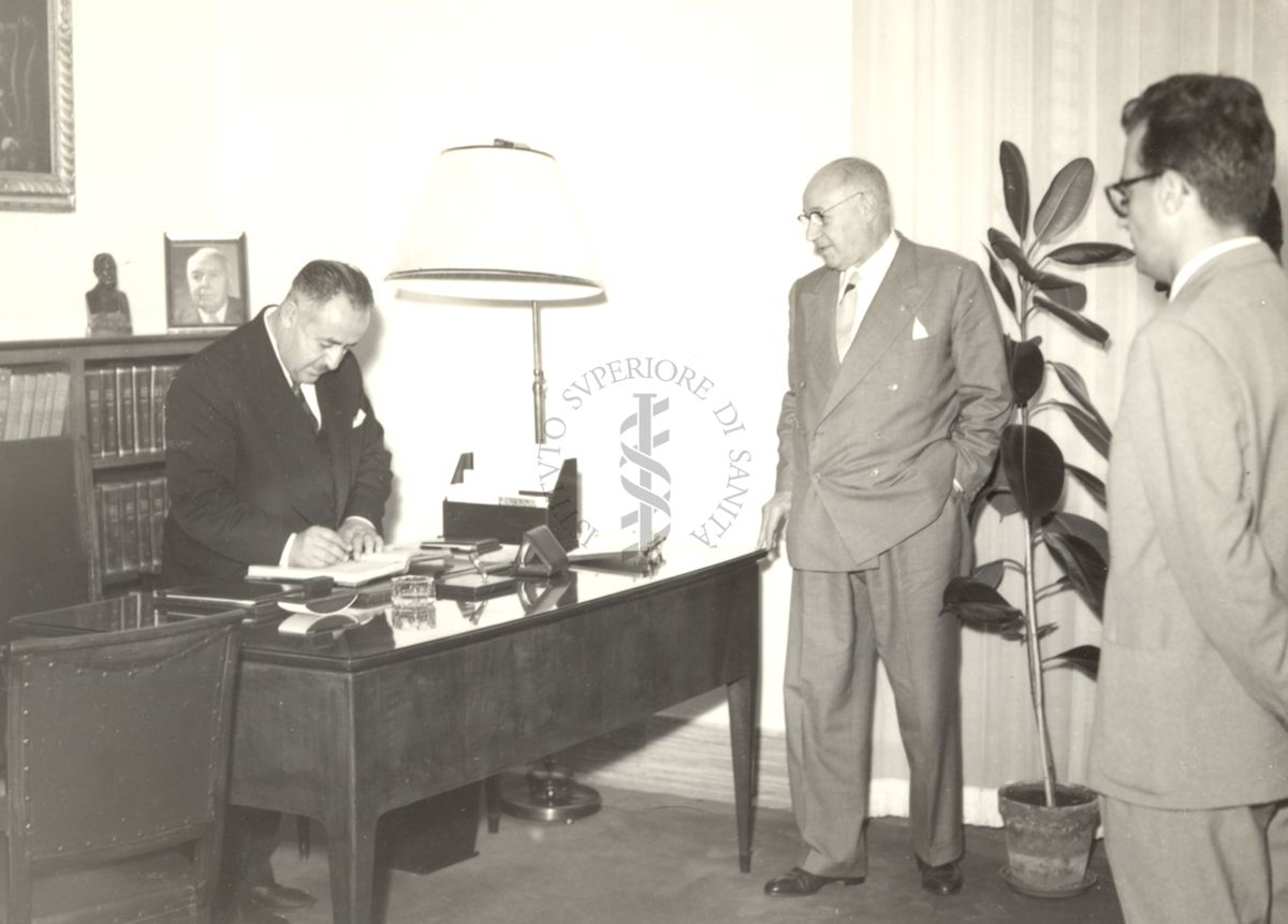 Il Ministro della Sanità della Cirenaica (a sinistra) firma alla scrivania di fronte al Prof. Domenico Marotta (su fondo al centro)