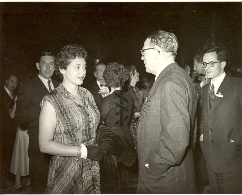 In primo piano una donna con guanti e cappotto tra le mani a colloquio con uomo con le mani in tasca durante il ricevimento in Campidoglio offerto dal Sindaco di Roma in occasione del VI Congresso internazionale di microbiologia. Sullo sfondo altri partecipantia l ricevimento.