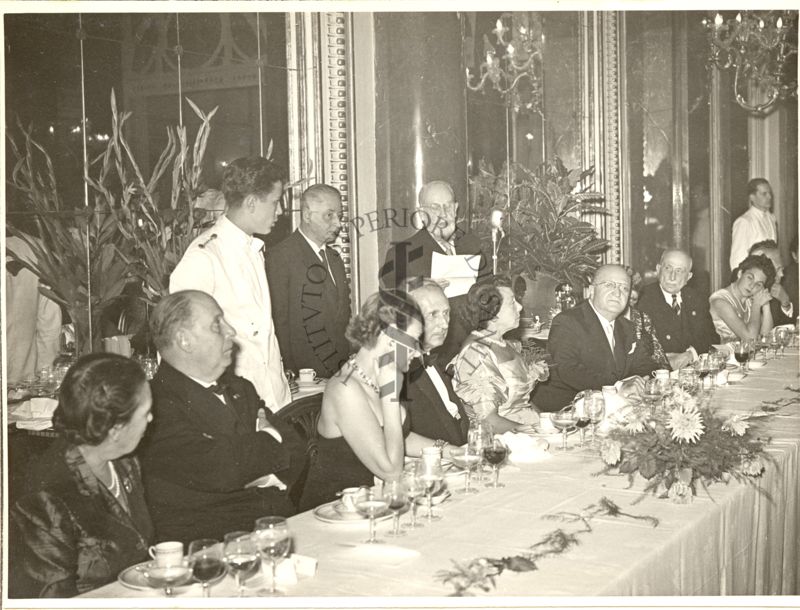 Ripresa del tavolo centrale durante il Pranzo al Grand Hotel di Roma in occasione del Congresso mentre un soggetto tiene un discorso dal microfono. Inquadrato il Sindaco di Roma Rebecchini (secondo da sinistra).