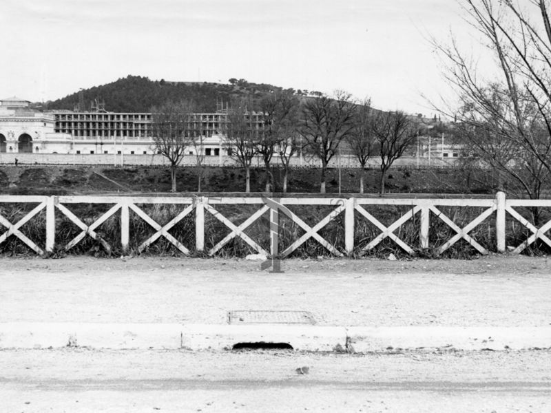 Inquadratura del marciapiede di una carreggiata che corre parallela al Tevere, con il Palazzo Littorio in costruzione sullo sfondo