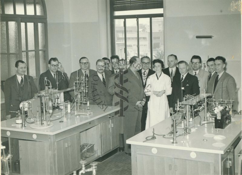 Foto di gruppo degli Ufficiali Veterinari francesi in visita presso l'istituto Superiore di Sanità dietro ai banconi di un laboratorio. Presente anche una dipendente dell'Istituto in camice