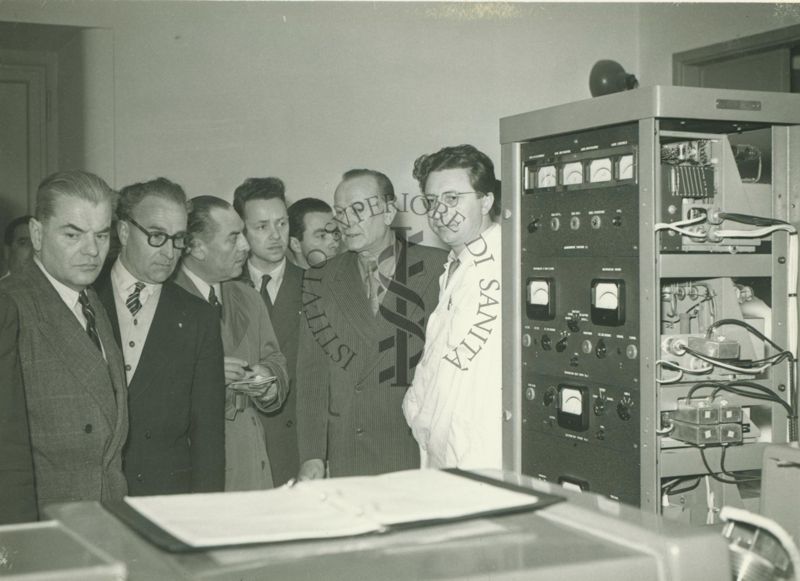 Foto di alcuni Ufficiali Veterinari francesi in visita presso l'istituto Superiore di Sanità davanti ad un'apaprecchiatura dell'Istituto. Presente anche un dipendente dell'Istituto in camice