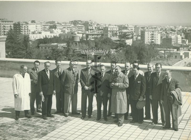 Foto di gruppo degli Ufficiali Veterinari francesi durante la visita all'Istituto Superiore di Sanità, ripresi dall'alto sulla terrazza dell'Istituto con una veduta di Roma sullo sfondo. Presente anche un dipendente dell'Isitituto in camice