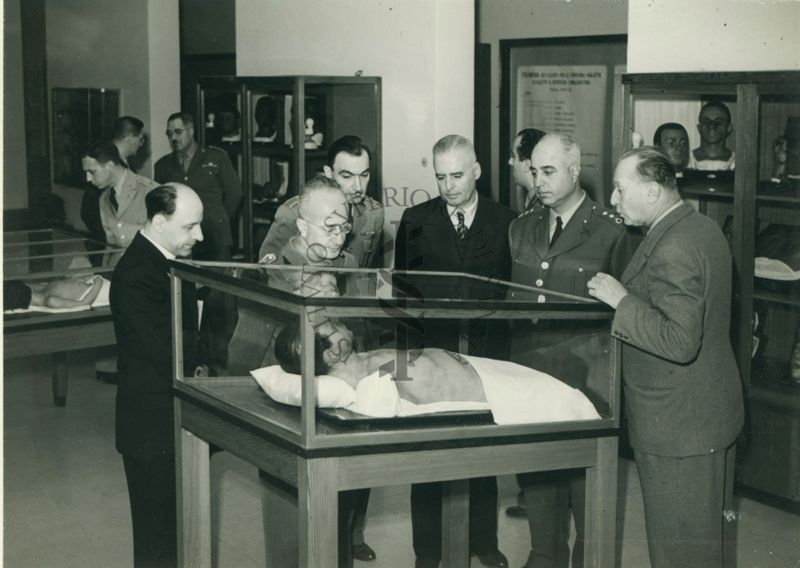 Gruppo Sei uomini, di cui tre in uniforme, ripresi frontalmente intorno ad una vetrina contenente il mezzo busto di un manichino raffigurante un uomo conservato all'interno dei locali dell'Istituto Superiore di Sanità. Si riconosce il Dott. Massimo Pantaleoni.