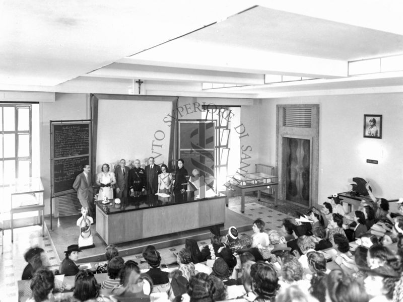 Inquadratura dall'alto del tavolo dei relatori a un corso, in un'aula dell'Istituto Superiore di sanità (attuale aula Marotta)