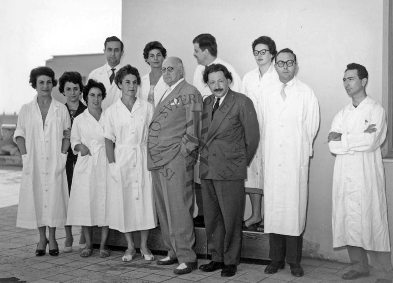 Foto di gruppo all'esterno dell'Istituto Superiore di Sanità, sulla terrazza dell'edificio centrale, con al centro il Prof. Ernst Boris Chain e il Prof. Domenico Marotta e, primo da sinistra, in seconda fila, il Prof. Francesco Pocchiari