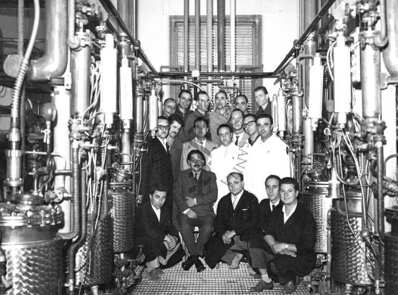 Foto di gruppo con al centro, seduto, il Prof. Ernst Boris Chain, all'interno dell'edificio che ospitava i fermentatori per la fabbricazione della penicillina