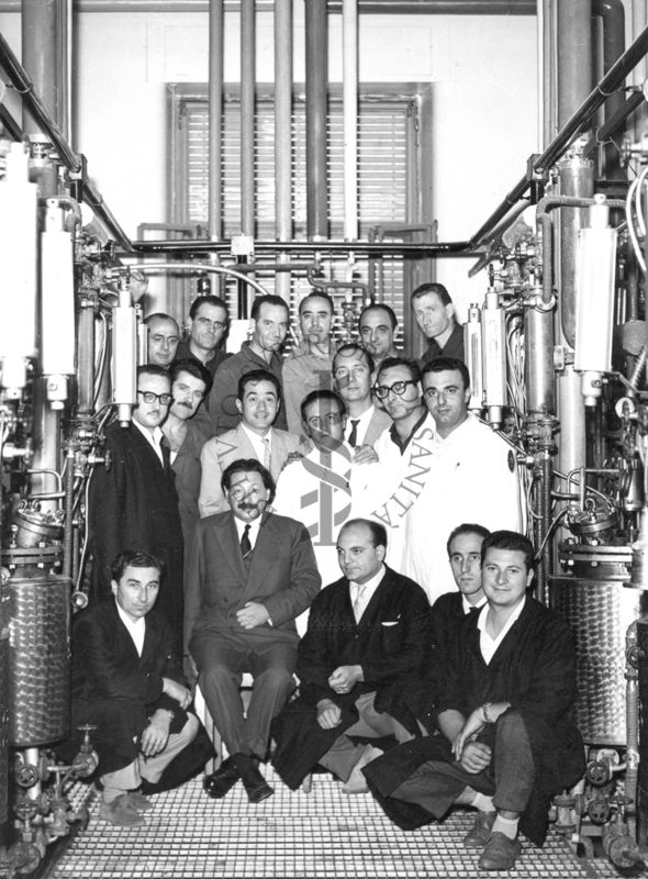 Foto di gruppo con al centro, seduto, il Prof. Ernst Boris Chain, all'interno dell'edificio che ospitava i fermentatori per la fabbricazione della penicillina