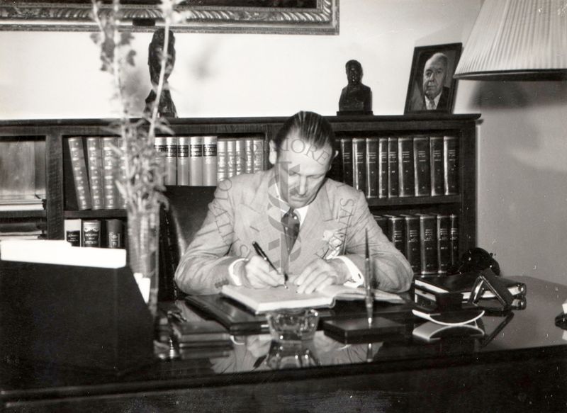 L'Ambasciatore Britannico Sir Ashley Clarke seduto, intento a firmare documenti alla scrivania del prof. Domenico Marotta