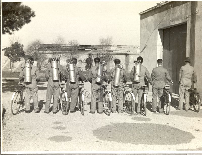 Squadra attrezzata di biciclette per la disinfestazione con D.D.T., fotografata di spalle