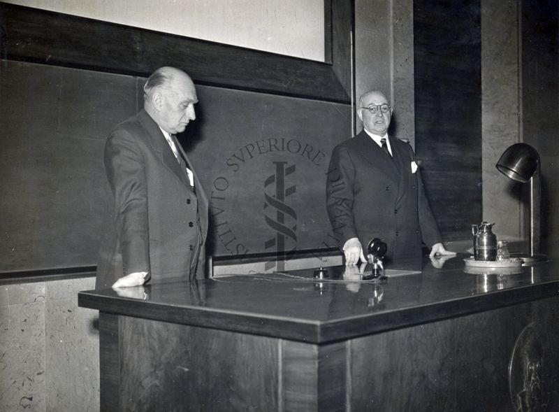 Il Prof. Heymaus (a sinistra) e il Prof. Domenico Marotta (a destra) in piedi dietro al tavolo dei relatori in occasione della Conferenza tenuta presso l'Istituto Superiore di Sanità