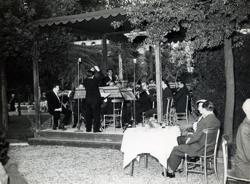 Foto dei musicisti e del loro direttore ripreso di spalle mentre suonano sotto un gazebo, nel giardino dell'Istituto Superiore di Sanità, in occasione del IX Congresso nazionale dell'industria agraria