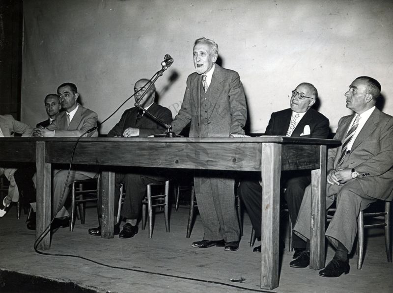 Uno dei relatori ripreso dietro al tavolo, intento a parlare al microfono, insieme ad altri ospiti. Seduto alla sua destra il Prof. Domenico Marotta, invitato a parlare alla conferenza presso l'Università Popolare Romana