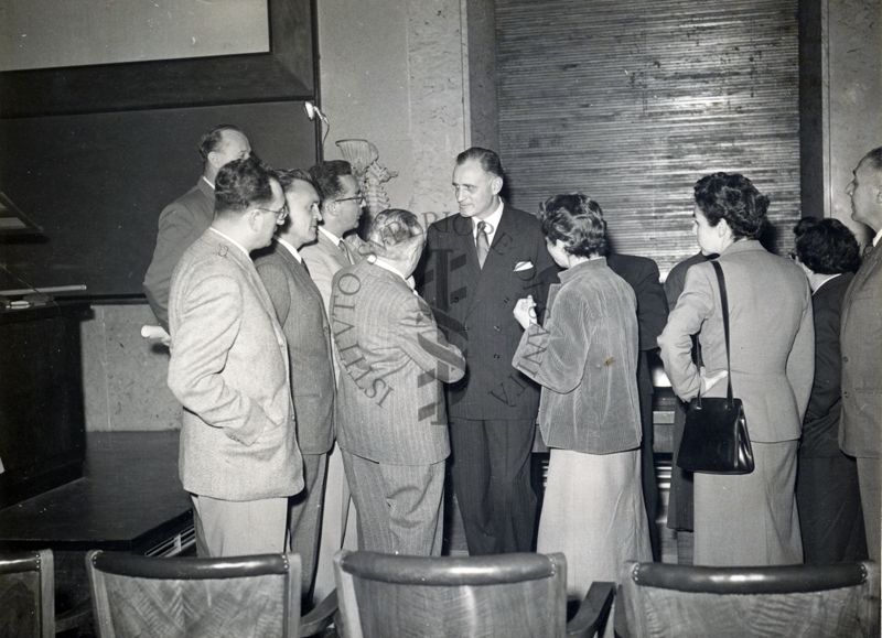 Il Prof. H. Corwin Hinshaw (al centro) circondato da un gruppo di persone, all'interno dell'aula magna dell'Istituto Superiore di Sanità al termine della sua conferenza