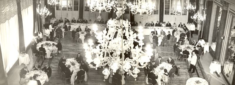 Ripresa dall'alto di una grande sala da pranzo con lampadari di cristallo e tavoli con persone sedute